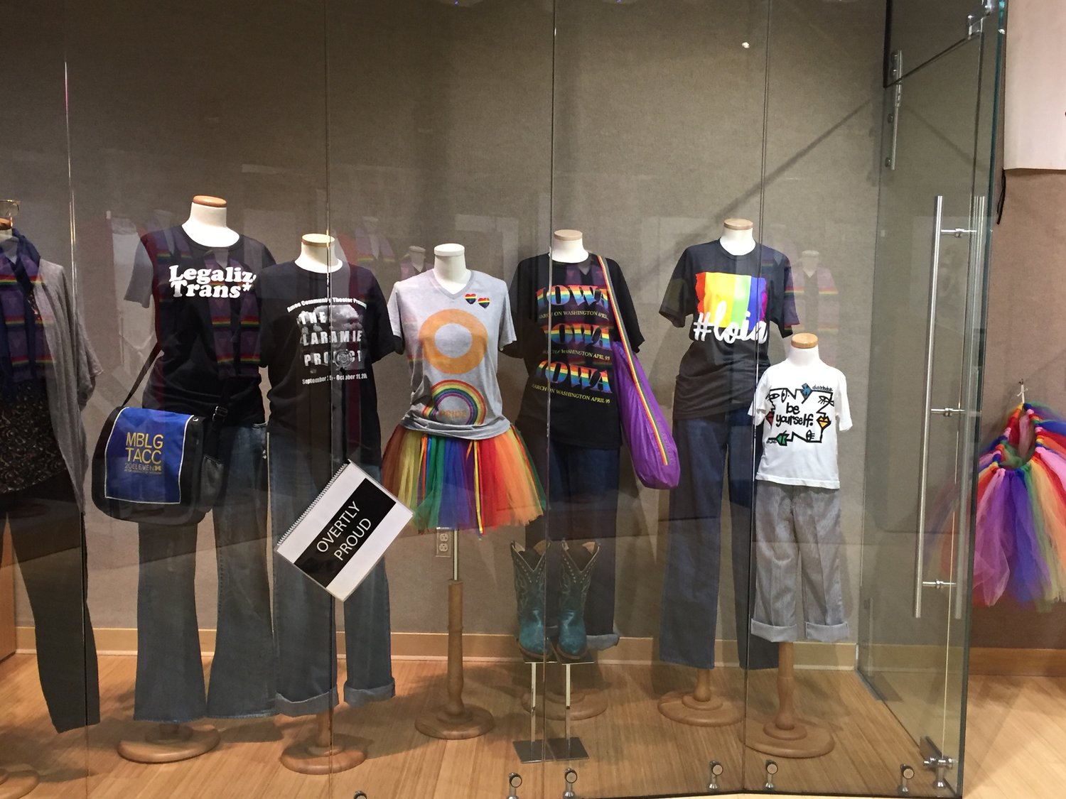 Dress forms displaying "Overtly Proud" outfits in glass exhibition case