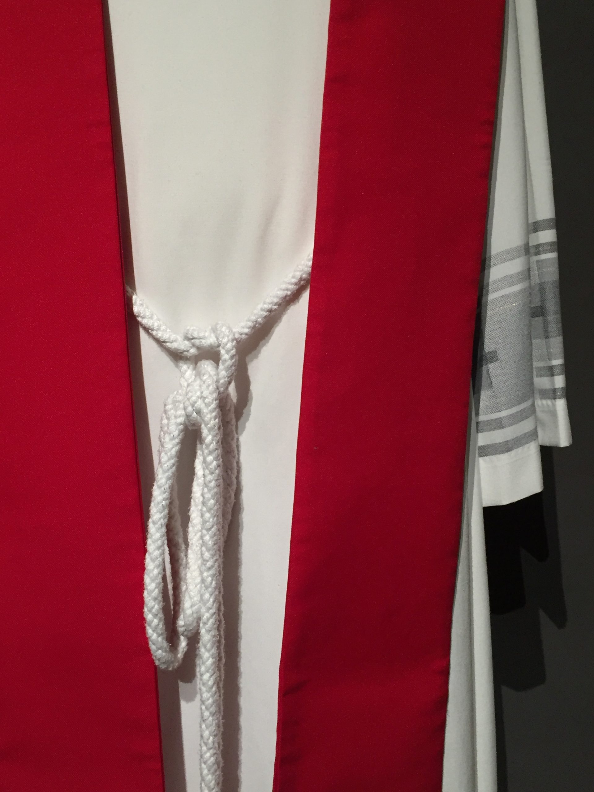 White long-sleeved alb, red stole with rainbow butterfly motif, white cincture