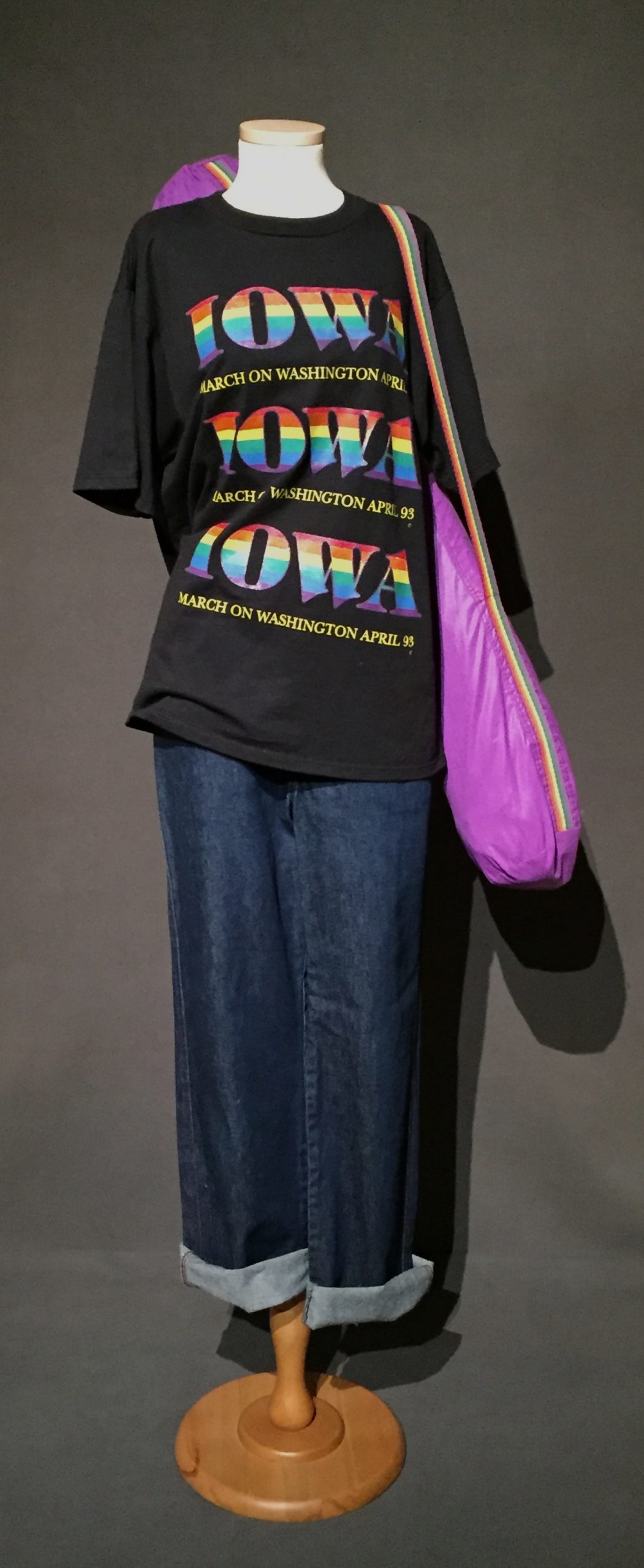 Black short sleeve t-shirt with rainbow lettering reading: "Iowa: March on Washington 93", cuffed denim pants, and purple bag with rainbow strap