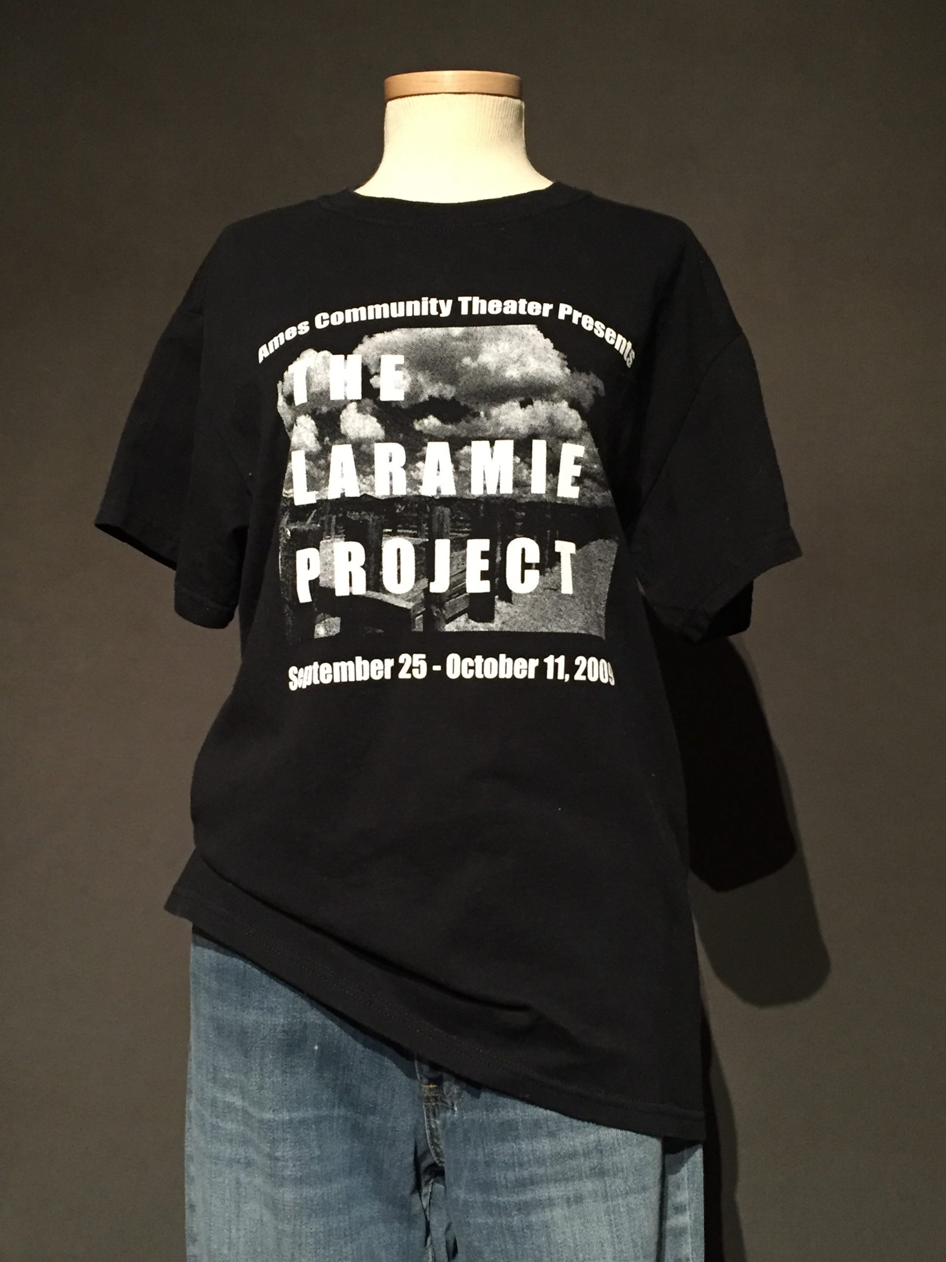 Black t-shirt with white text reading: "Ames Community Theater Presents: The Laramie Project, September 25-October 11, 2019"