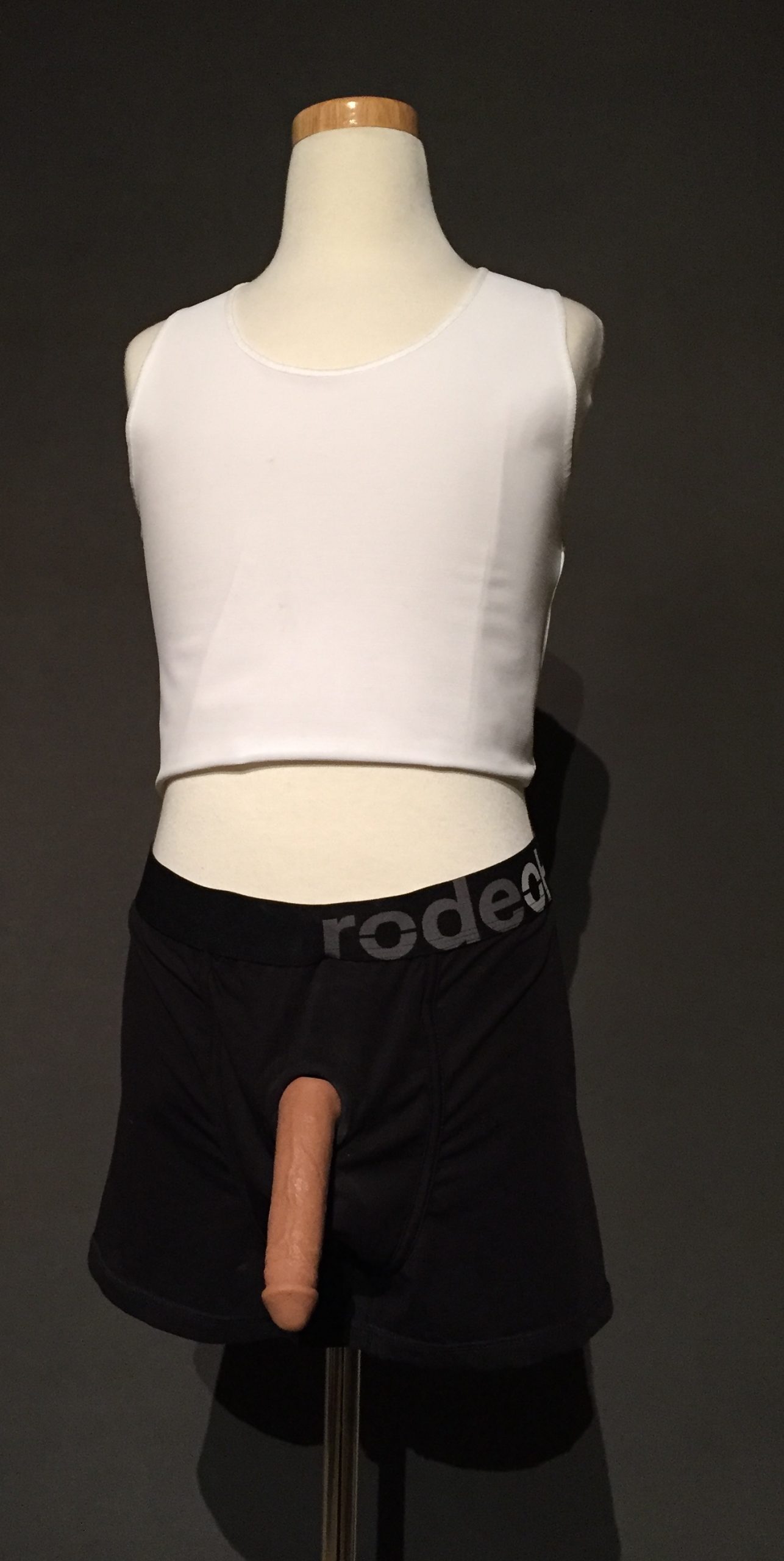 White binder, black packing underwear, realistic-looking silicone prosthetic penis AKA packer with light-medium skin tone