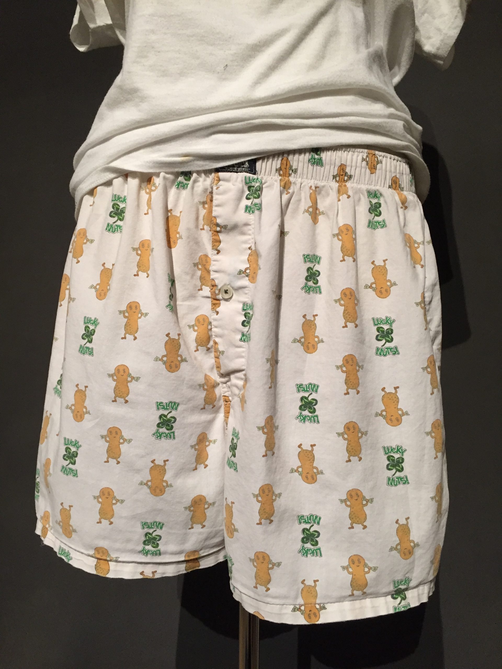 Close-up of white boxer shorts with print featuring peanuts and four-leaf clovers with text reading: "Lucky Nuts" paired with white t-shirt