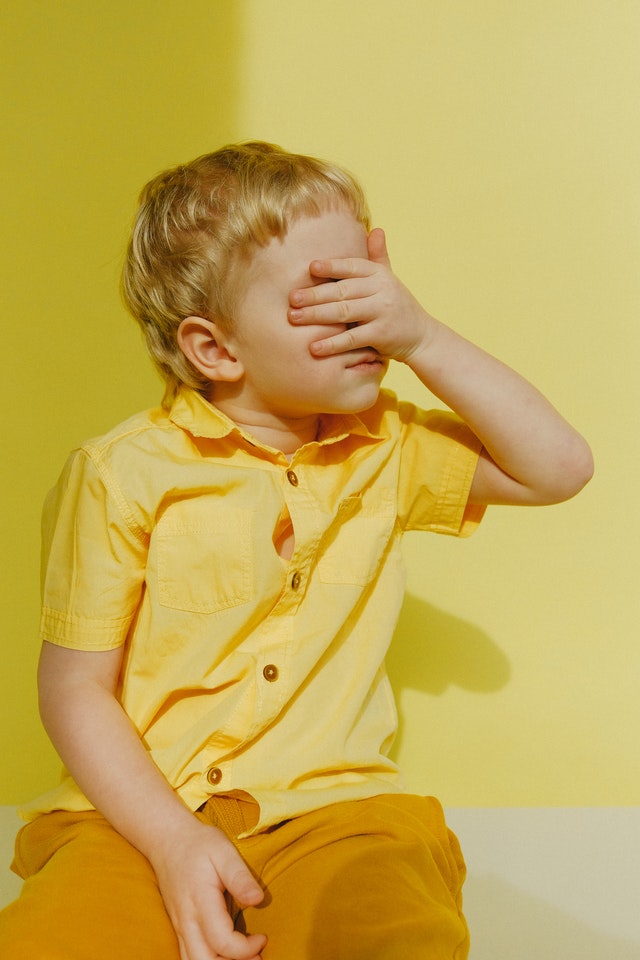 A young boy with a hand over his eyes.