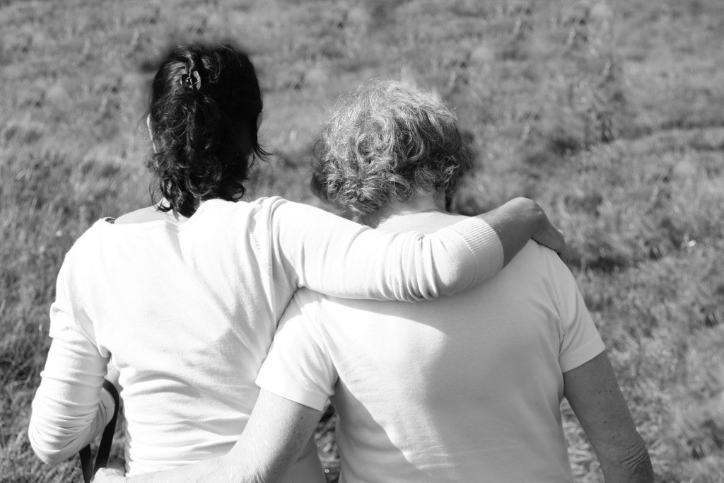 black and white photo with two people whose arms are around one another, heads down.