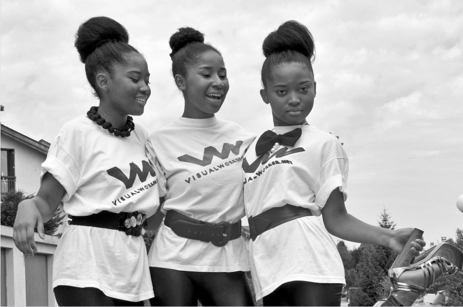 Black and white photo of three teenage Black girls posing for the camera in matching outfits.