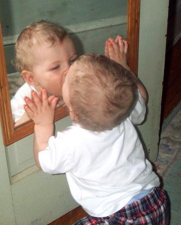 A photo of a baby kissing his reflection in a mirror