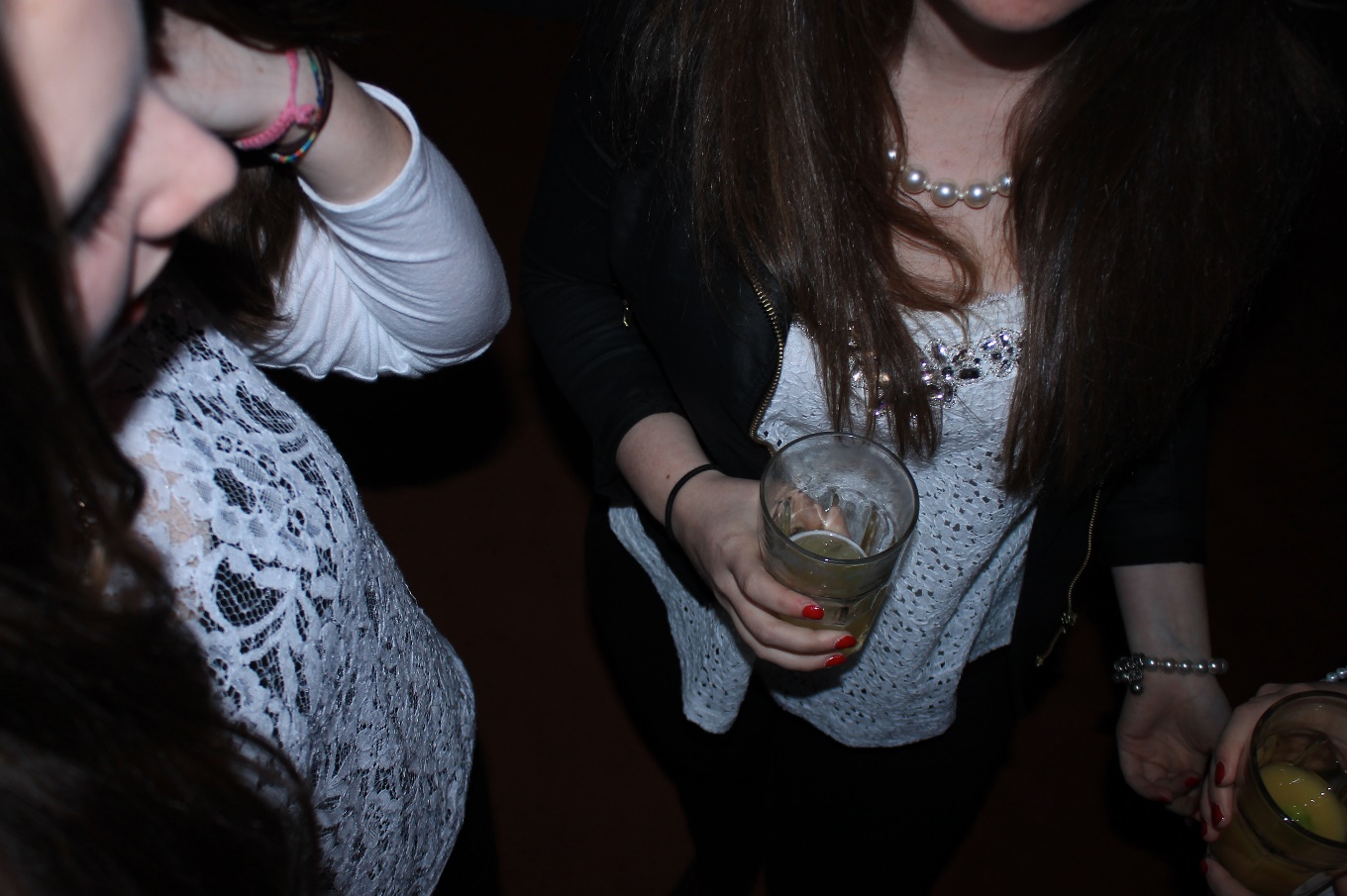 Photo of two girls holding drinks in a dark room.