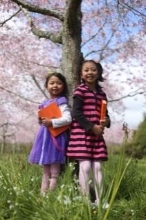 Photo of two young girls holding books by a tree