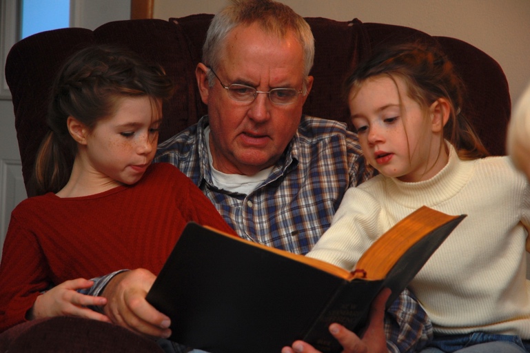 Photo of an older man reading to two children.