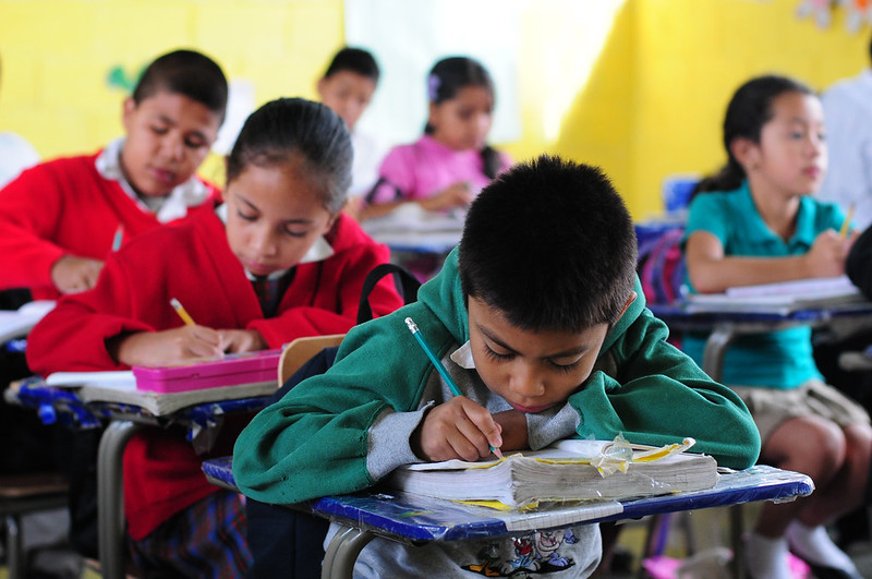 Children looking down at books in a classroom and writing.