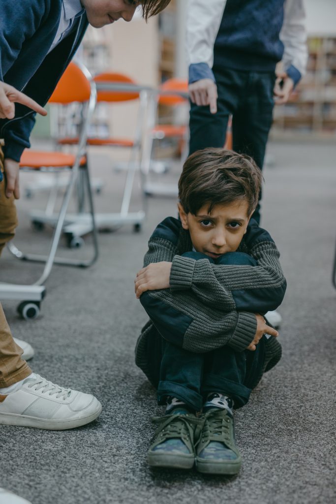 Photo of a sad boy sitting on the floor of a classroom.