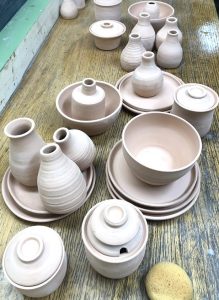 An assortment of wheel-thrown pottery, including unglazed bowls, plates, and vases, stacked across a worn table