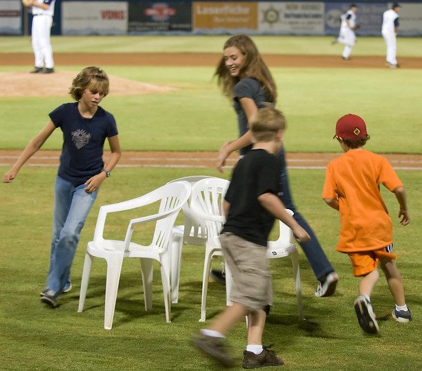 Four children run around 3 chairs in a game of musical chairs