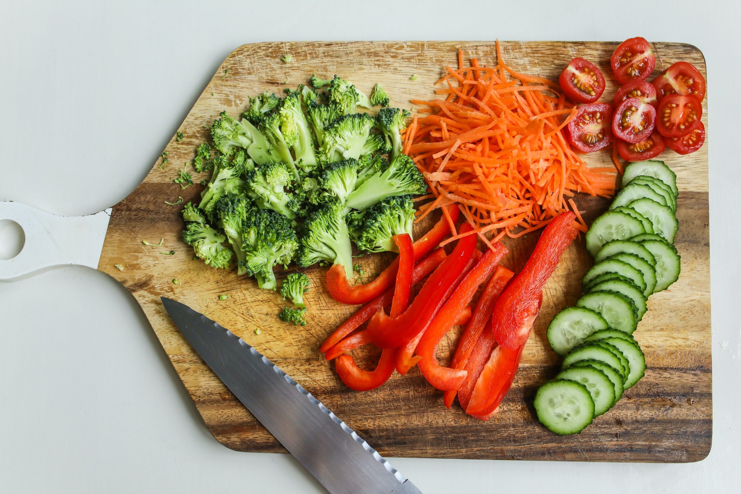 Photo of brocooli, tomatoes, carrots, and cucumber chopped on a cutting board