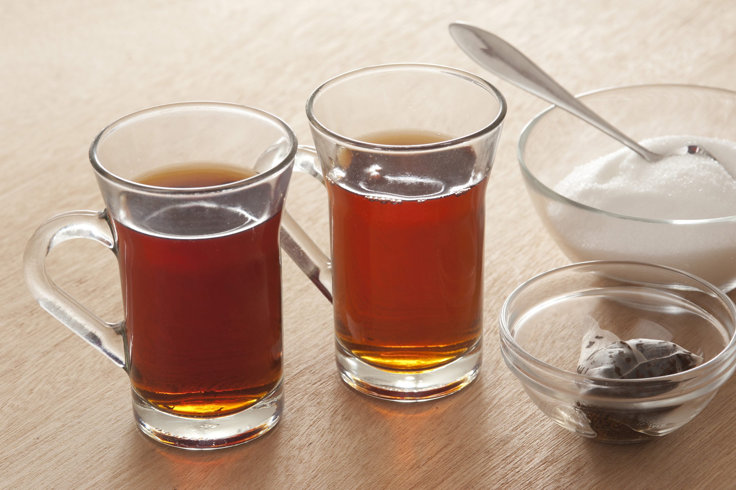 Hot black tea for two served in glass mugs with a bowl of sugar and the used teabags in a small dish