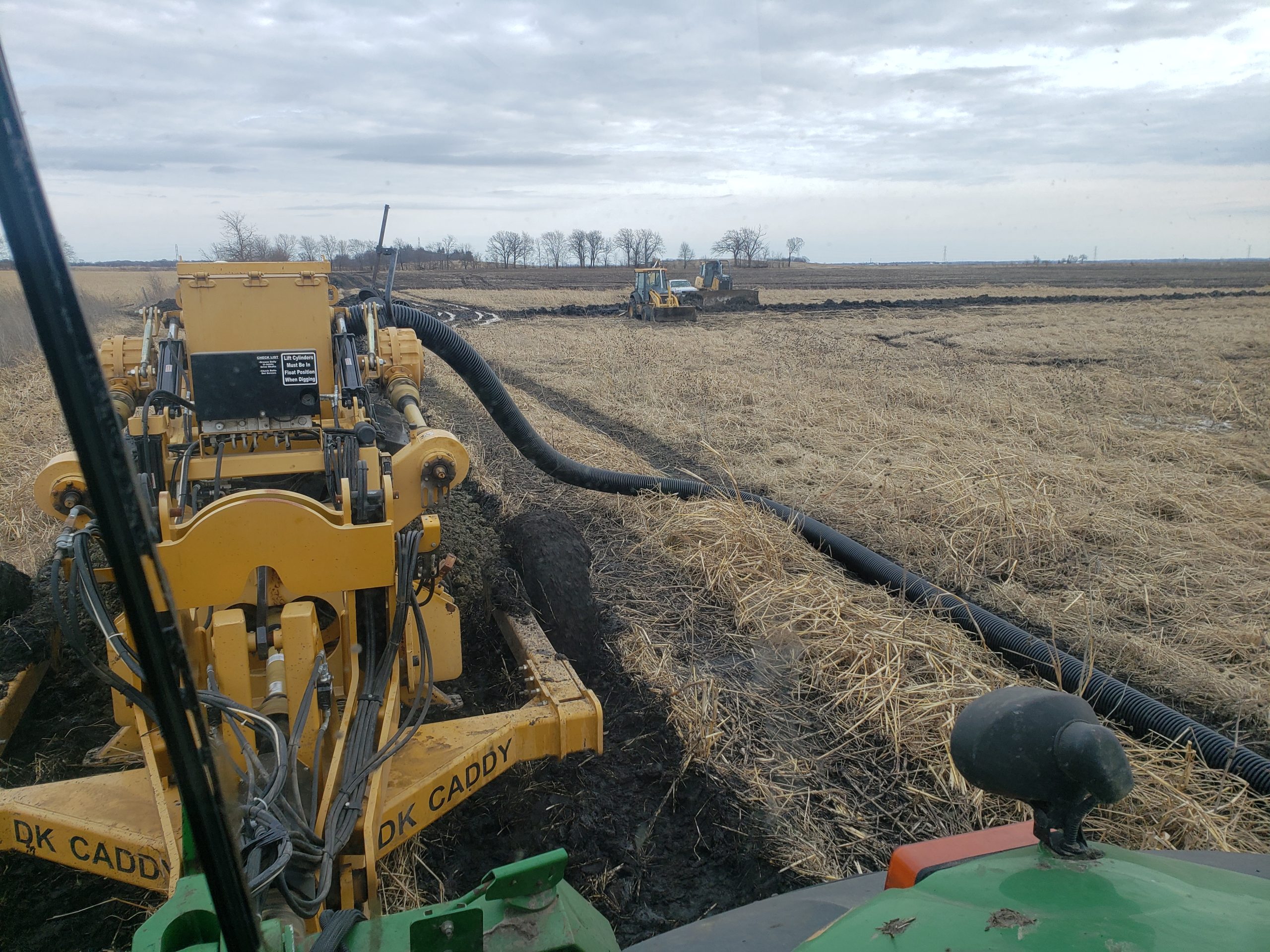 Photo of a tractor laying plastic pipes in a field.