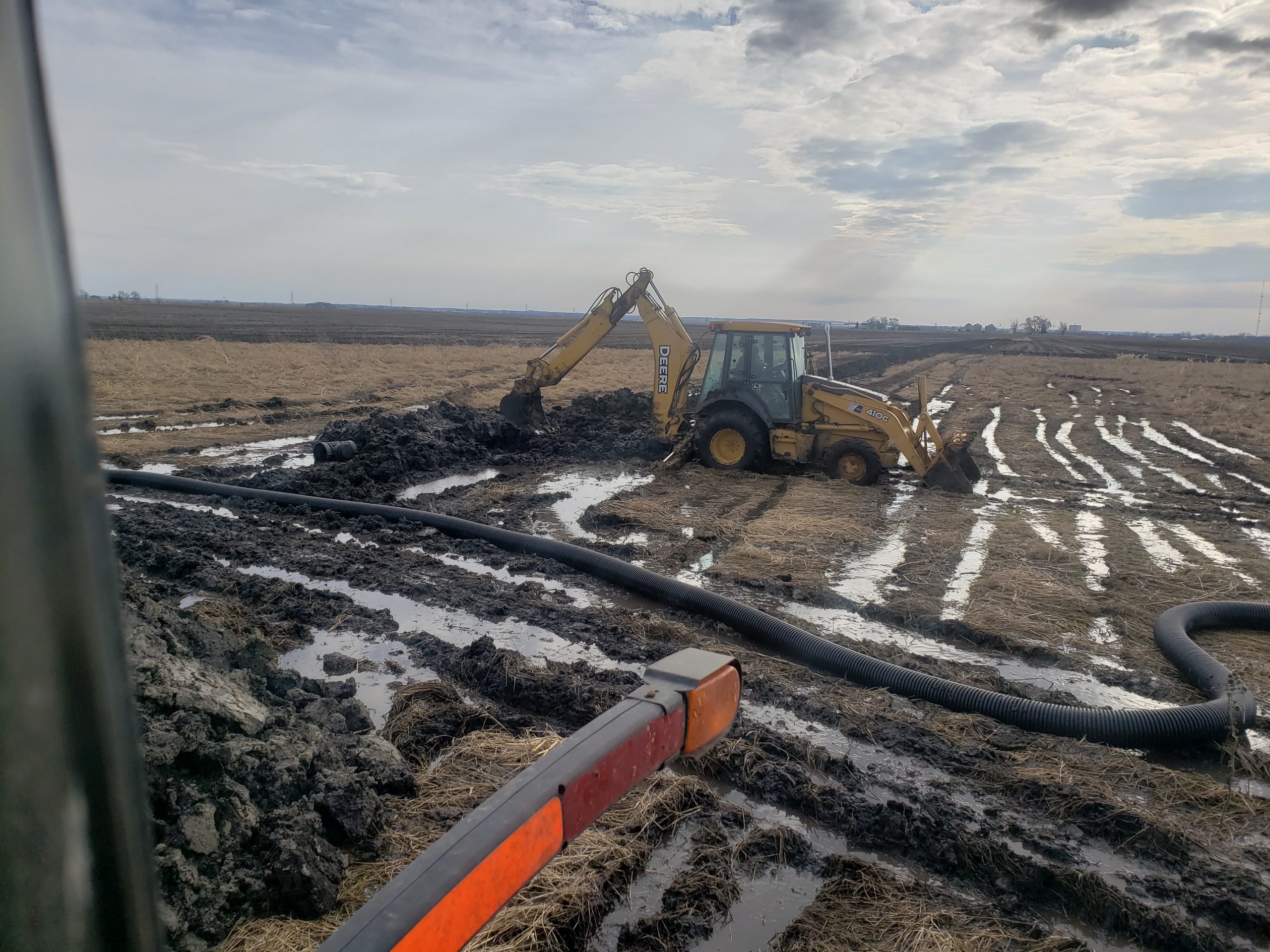 Photo of a tractor digging up a field with pooling water throughout its tracks.
