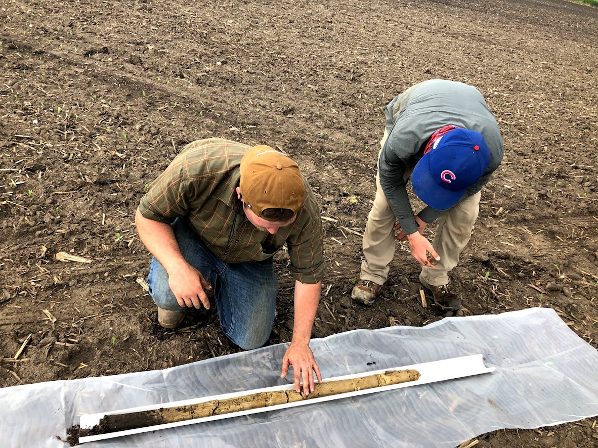Two students kneeled down looking at a very dry soil sample.