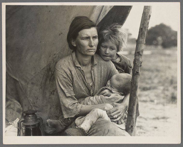 A black and white photo of a woman looking forward with a stern face, holding an infant while a young boy hangs his head on her shoulder.