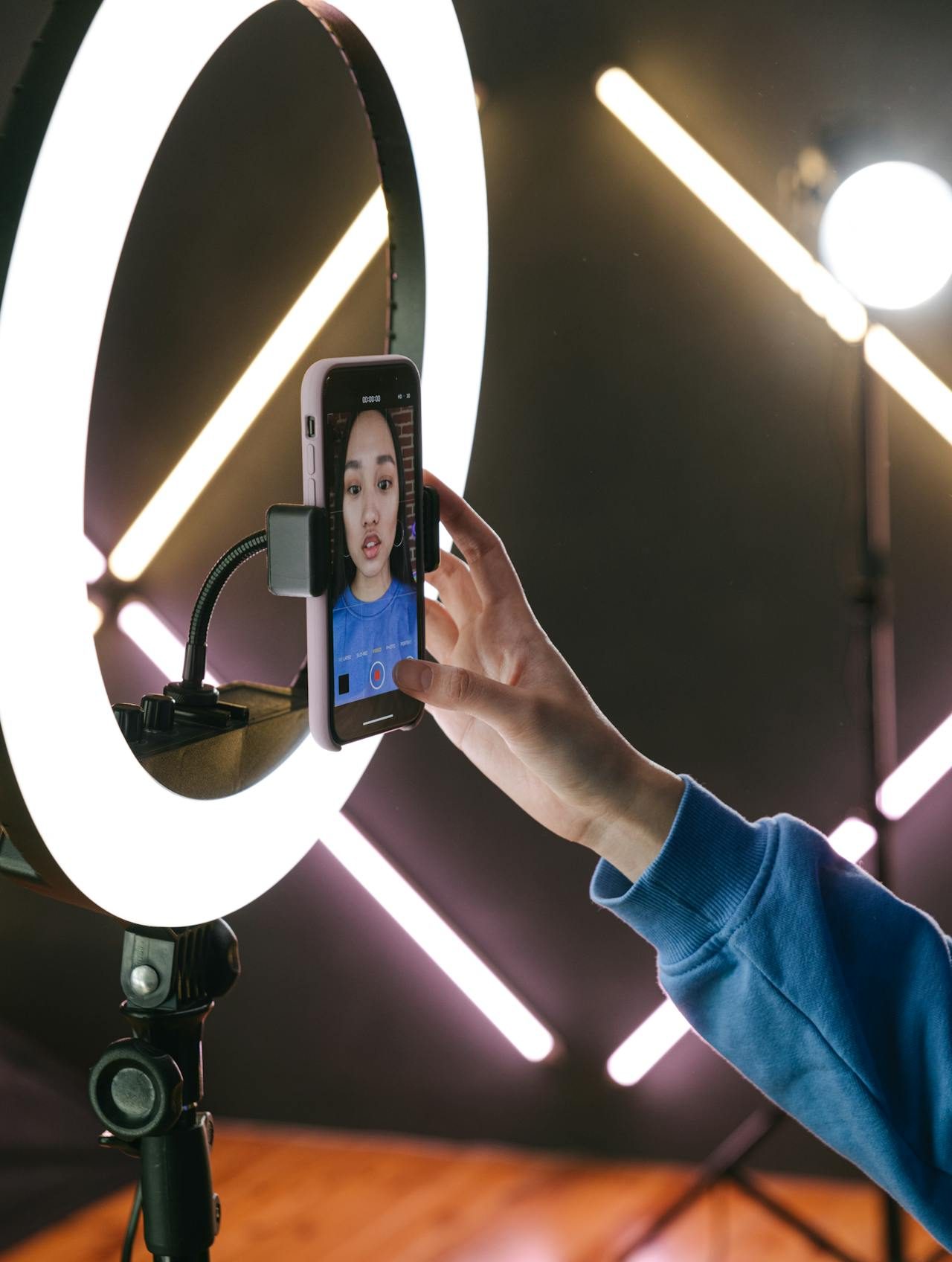 A photo of a young woman recording a video on her phone in front of a ring light.