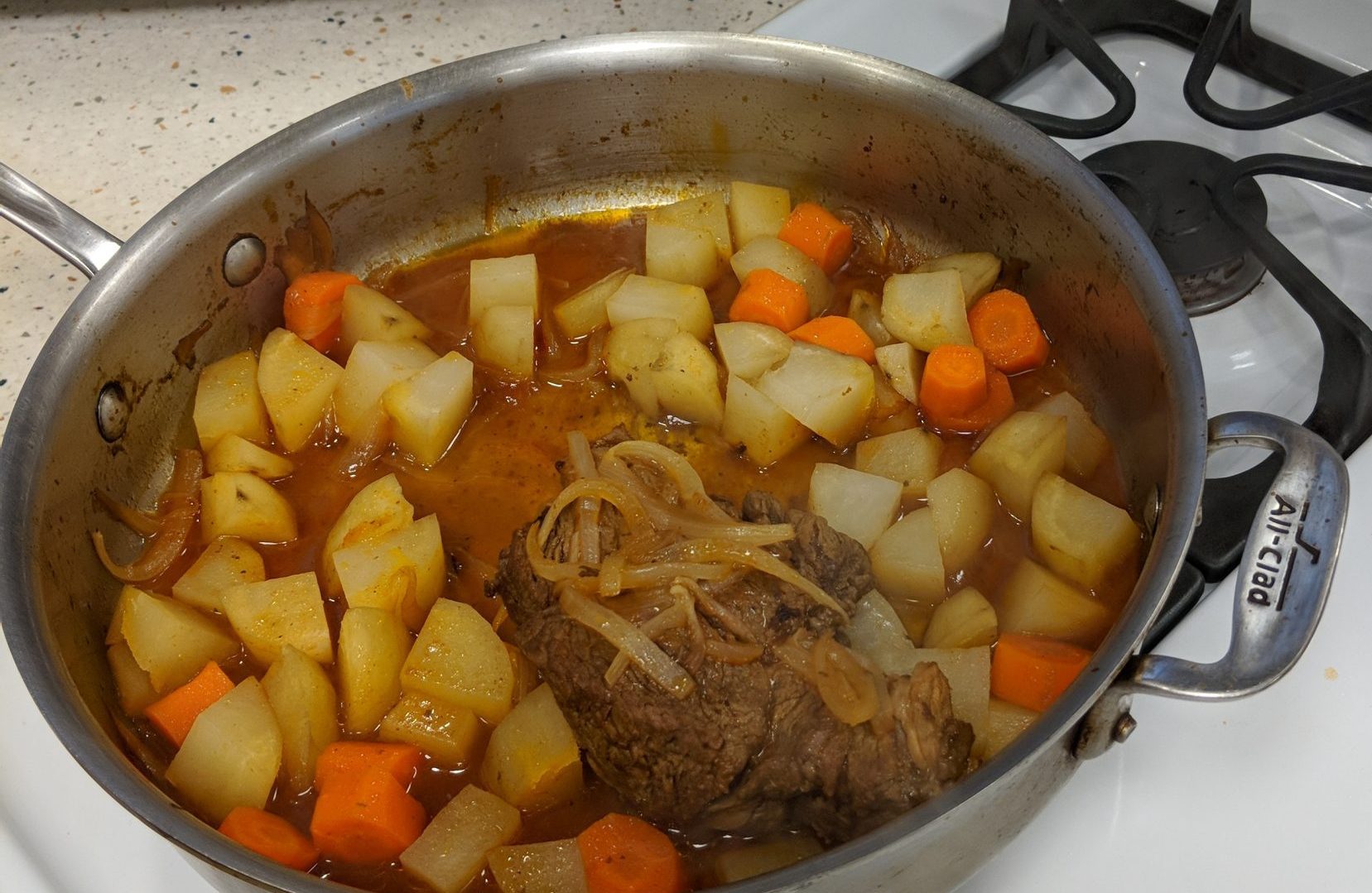 Stewed meat in a pan with potatoes, onions, carrots, and broth.