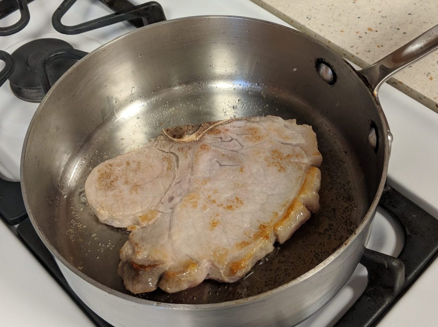 A piece of meat cooking in a dry saute pan.