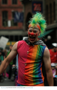 A person wearing the six-stripe rainbow shirt and makeup as a clown