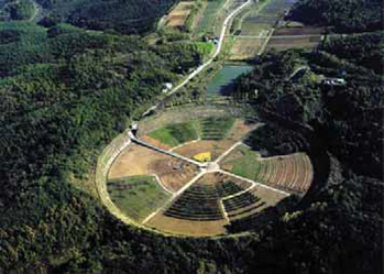 A photo of a large circular field with rows of crops at the end of a long road.